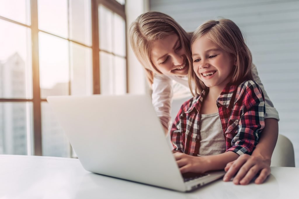 Beautiful young woman and her little cute daughter are using laptop at home. Enjoying spending time together.