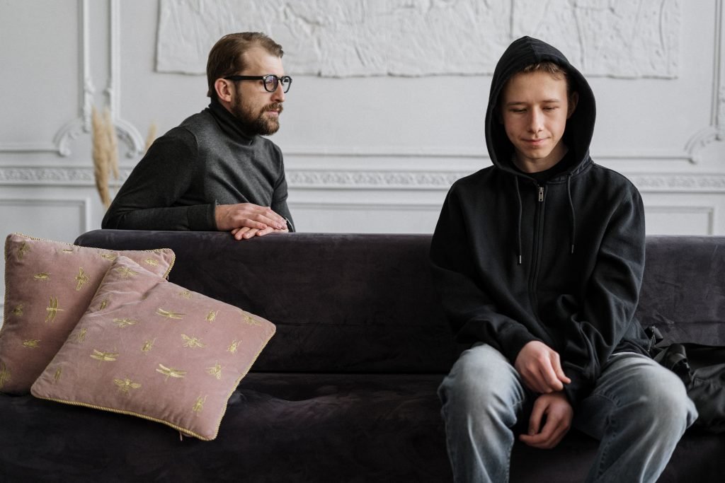 Image of an upset teen boy on a couch with his worried father looking at him. Overcome conflict in your family with family therapy in Englewood, CO.