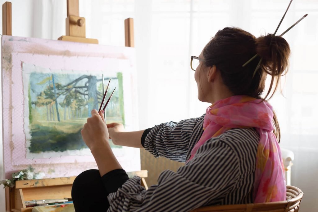 Image of a happy woman painting a forest picture on canvas. Discover how neurofeedback therapy for ADHD in Englewood, CO can help you effectively manage your symptoms.