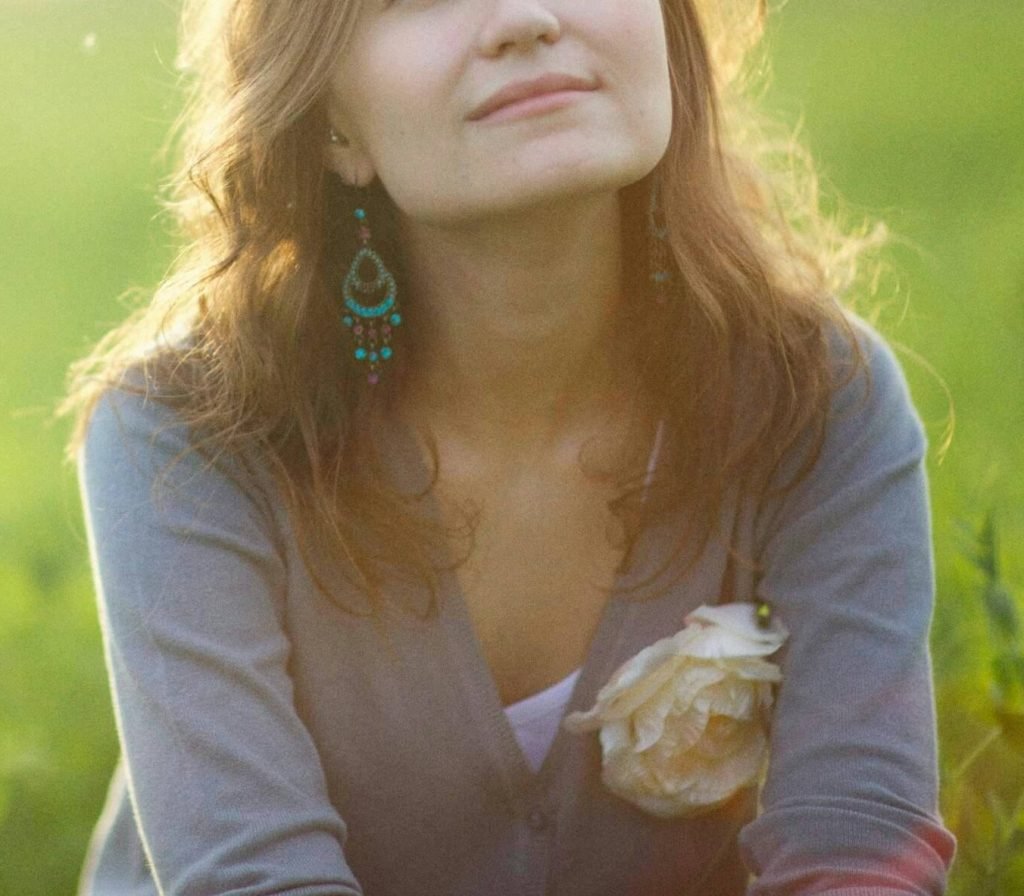 Image of a young woman sitting in the grass smiling as the sun shines on her. Overcome your mental health challenges with the help of neurofeedback therapy in Denver, CO.