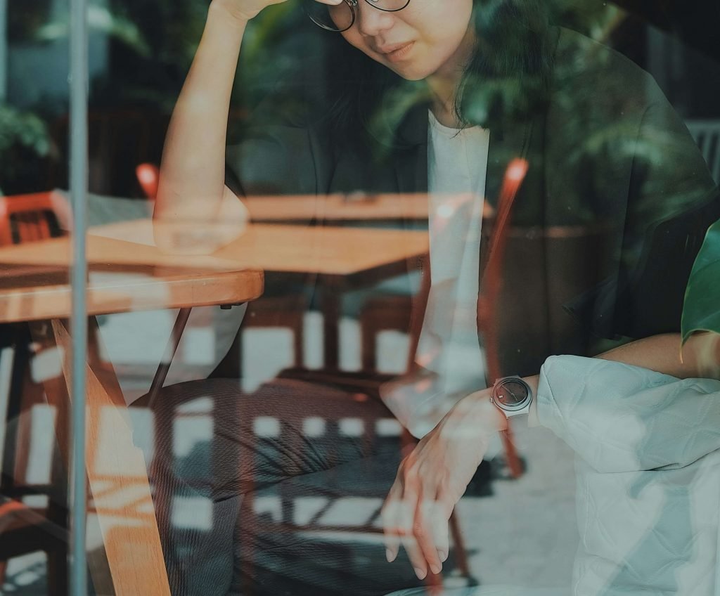 woman at table | emdr therapy in denver, co | emdr therapist in denver, co | emdr trauma therapy | emdr for ptsd | online therapy in colorado | 80127 | 80128 | 80124 Image of an upset woman behind a window sitting at a table in a cafe. Learn how EMDR therapy in Denver, CO can help you cope and work to improve your trauma symptoms.
