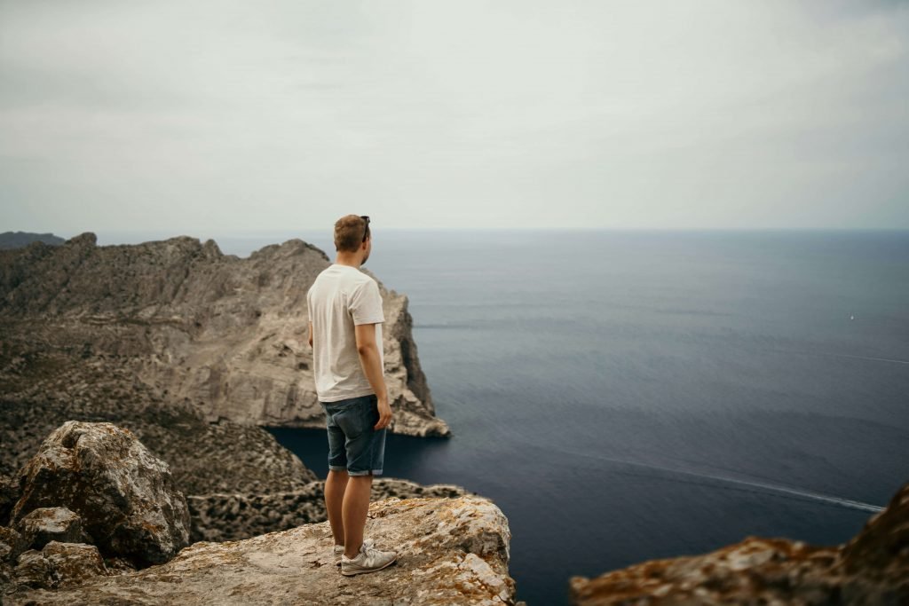 man on cliff | emdr therapy in denver, co | emdr therapist in denver, co | emdr trauma therapy | emdr for ptsd | online therapy in colorado | 80125 | 80121 | 80110 Image of a man standing on top of a rocky cliff overlooking the ocean on a cloudy day. Begin healing and managing your past trauma symptoms with the help of EMDR therapy in Denver, CO.