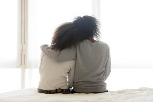 A mother and teen sit on the edge of a bed while hugging one another. This could represent the bonds cultivated after working with a relationship therapist in Englewood, CO. Search for a family therapist in Englewood, CO to learn more about the benefits of family therapy in Englewood, CO today. 