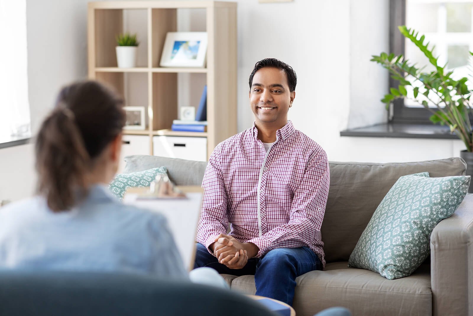 An adult man smiles while meeting with a therapist on a couch, discussing results of autism testing in Greenwood Village, CO. This supportive session focuses on next steps for autism treatment for adults in Colorado with an experienced autism therapist in Greenwood Village, CO. 