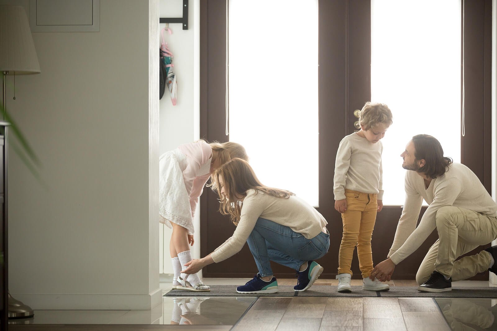 Two parents kneel down to help their young children put on shoes near the front door, working together through a busy morning transition. Everyday moments like this can feel especially overwhelming for parents with ADHD, but support is available. ADHD therapy for adults in Englewood, CO helps parents develop routines and external structures that make these transitions feel more manageable for the whole family. 