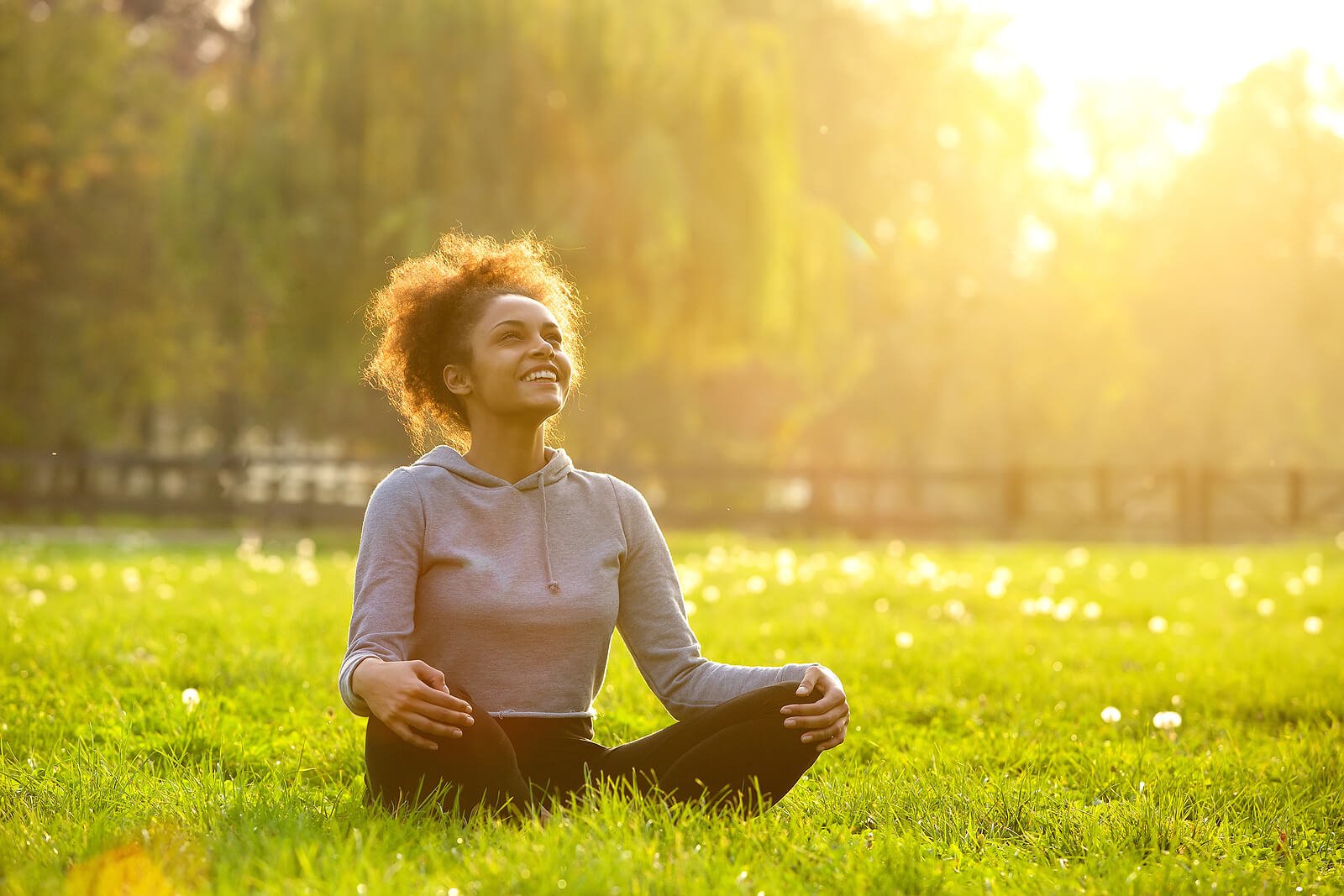 A young woman sits cross-legged in a sunlit grassy field, smiling and looking upward with a relaxed, open expression — a powerful image of the emotional regulation, improved focus, and inner calm that neurofeedback englewood clients work toward over the course of treatment. This is what recovery and regulation can feel like: not just the absence of symptoms, but a genuine sense of ease and presence. Whether you're seeking neurofeedback therapy in Englewood, CO for ADHD, anxiety, sleep issues, or another condition, this kind of transformation is what the process is designed to support. 